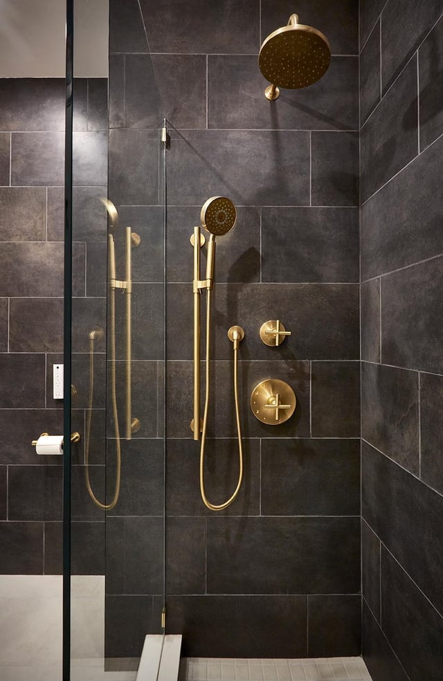 Modern shower with gold fixtures and dark tile walls.