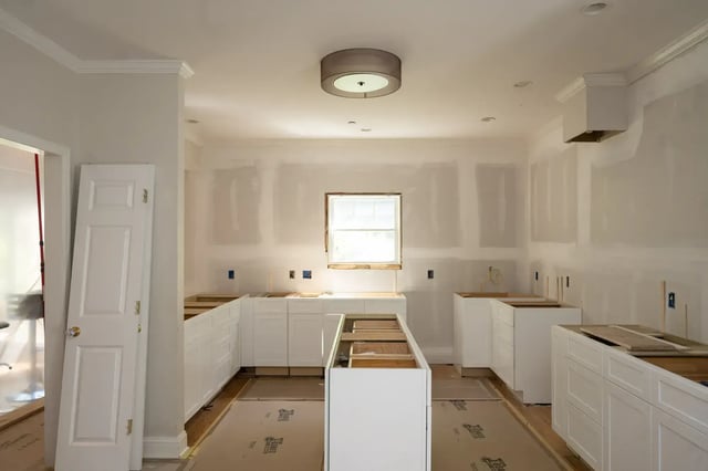 Kitchen under renovation with white cabinets and drywall.