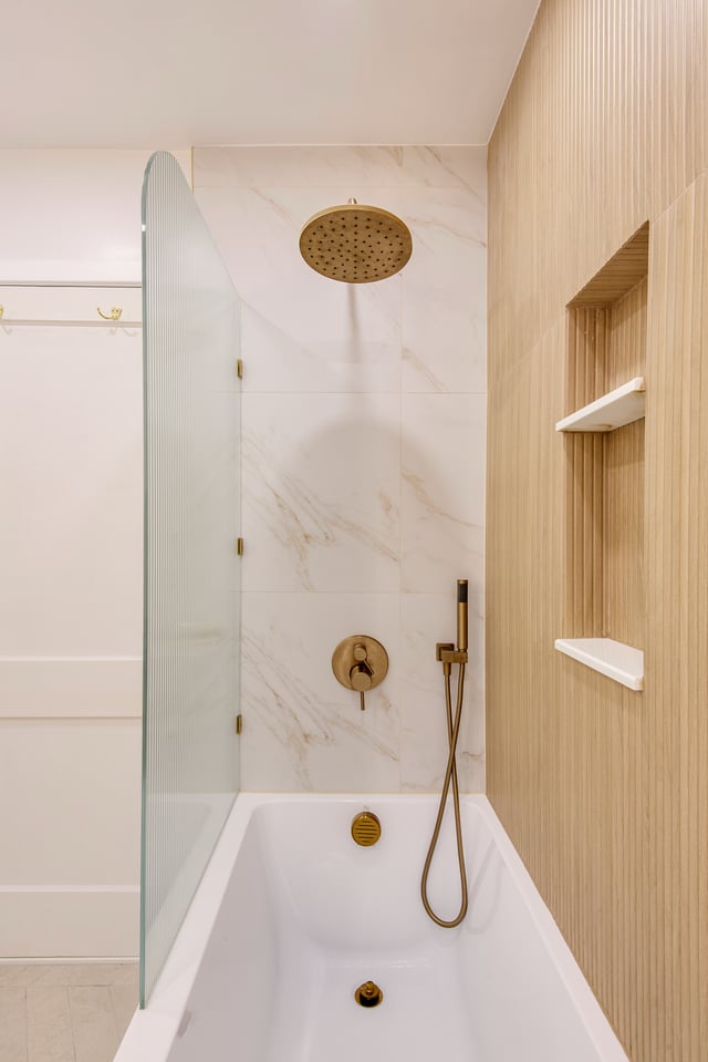 Modern bathroom with bathtub, gold fixtures, and glass shower screen.