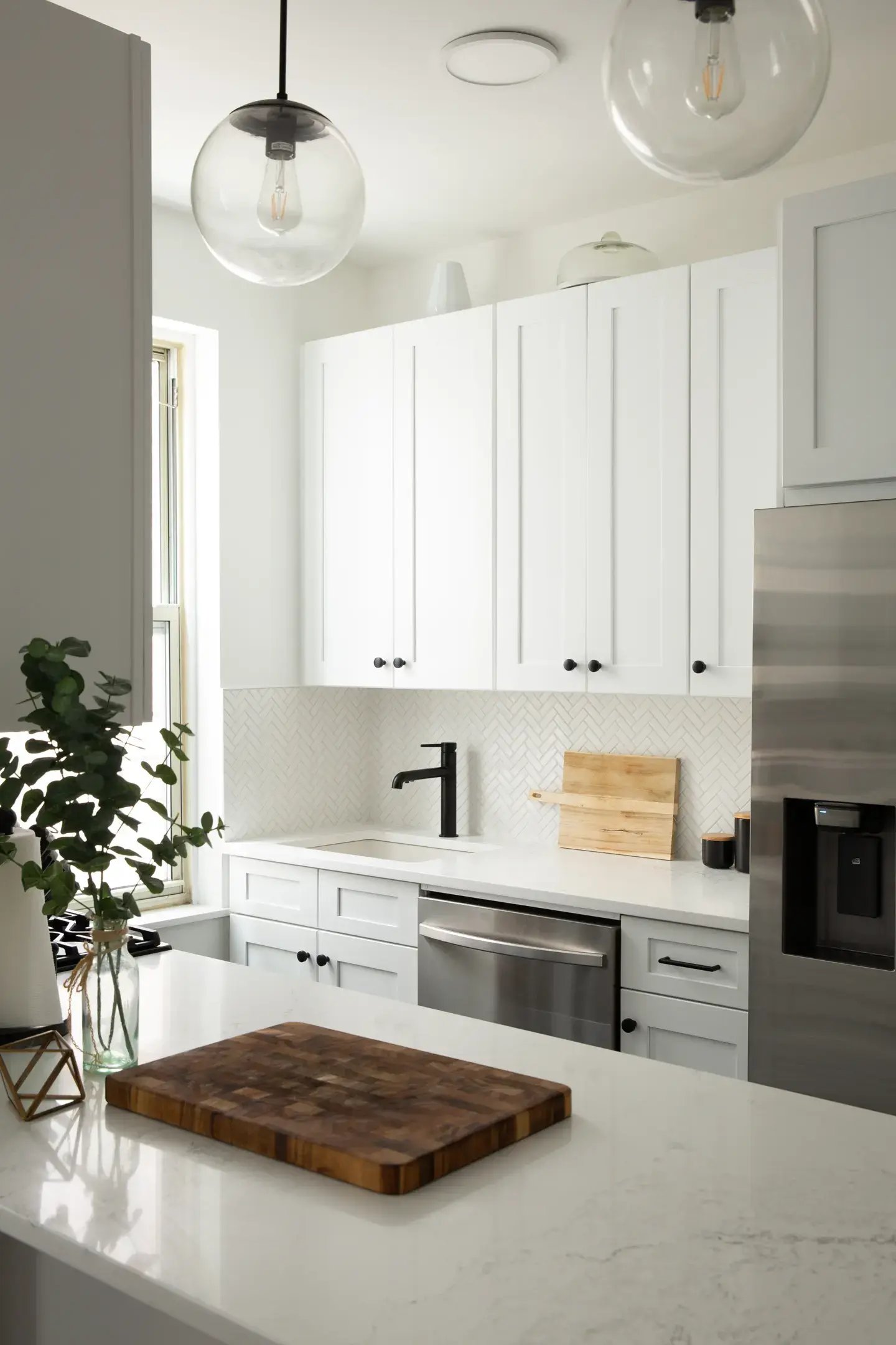 White kitchen with black faucet, wood board and glass lamps.