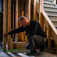Man measuring a wood wall frame next to a basement staircase.