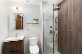 A modern bathroom featuring a wooden vanity, toilet, and glass-enclosed shower with dark tile.