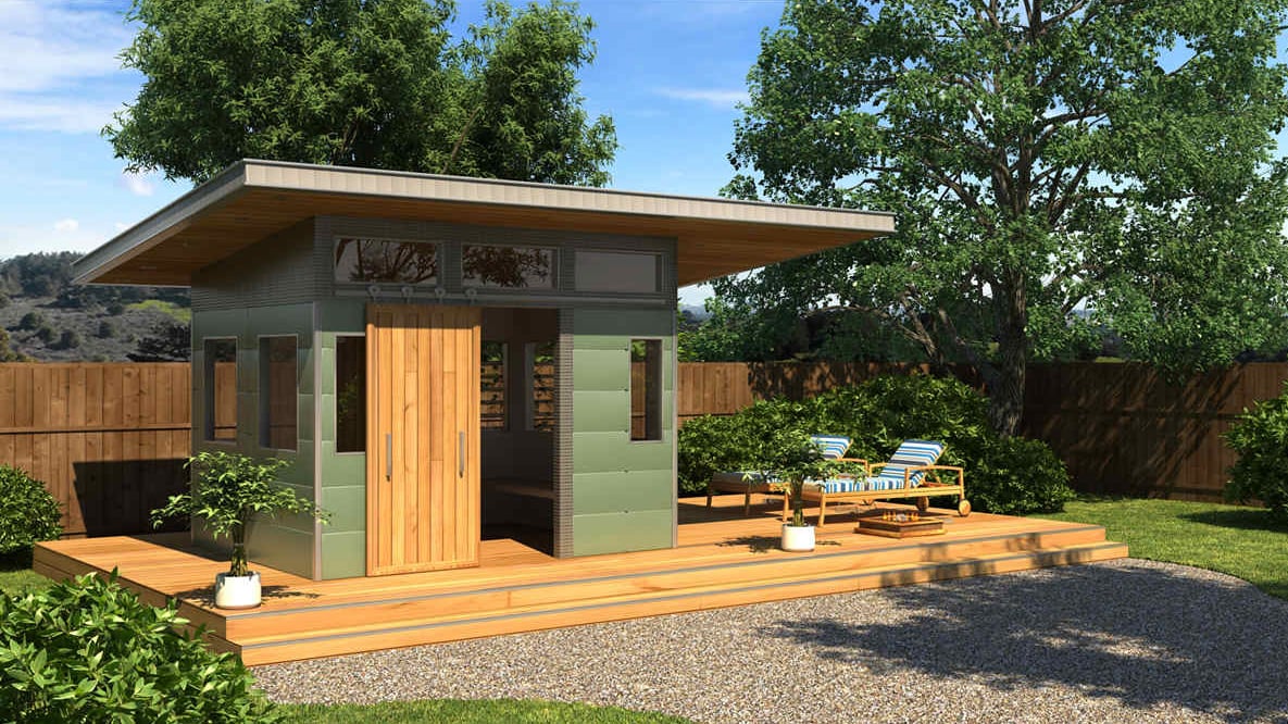  A compact, modern studio shed featuring sage green paneling, a natural wood sliding barn door, and a flat overhanging roof.