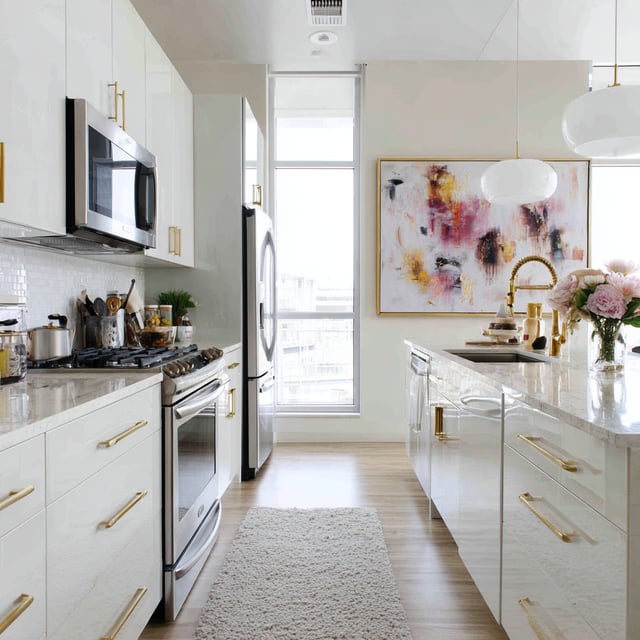 A modern, high-gloss white kitchen characterized by a bright, airy aesthetic and luxurious gold accents.