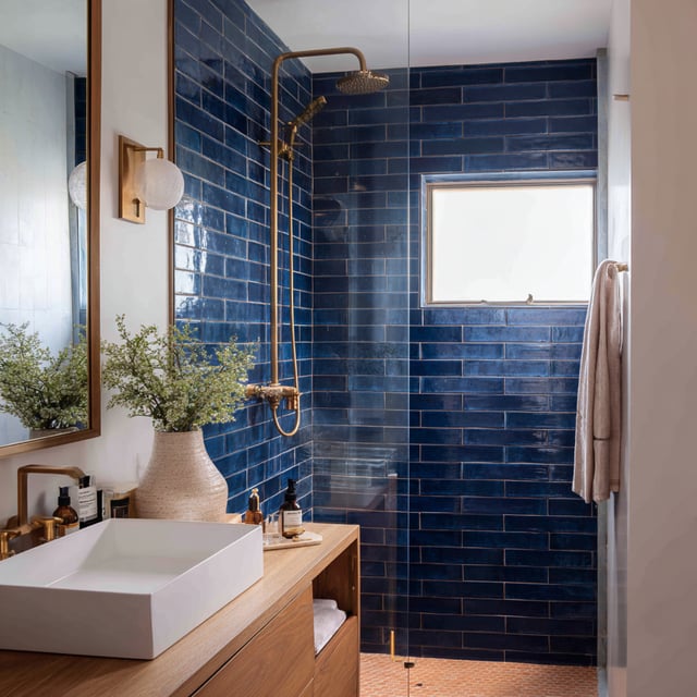 Blue bathroom with deep sea tile, gold shower, and a vanity.