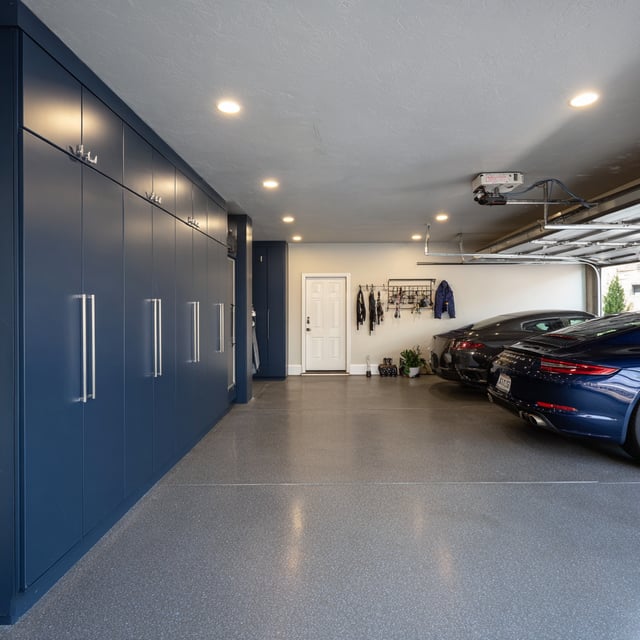  Renovated garage with blue cabinets and two parked cars.