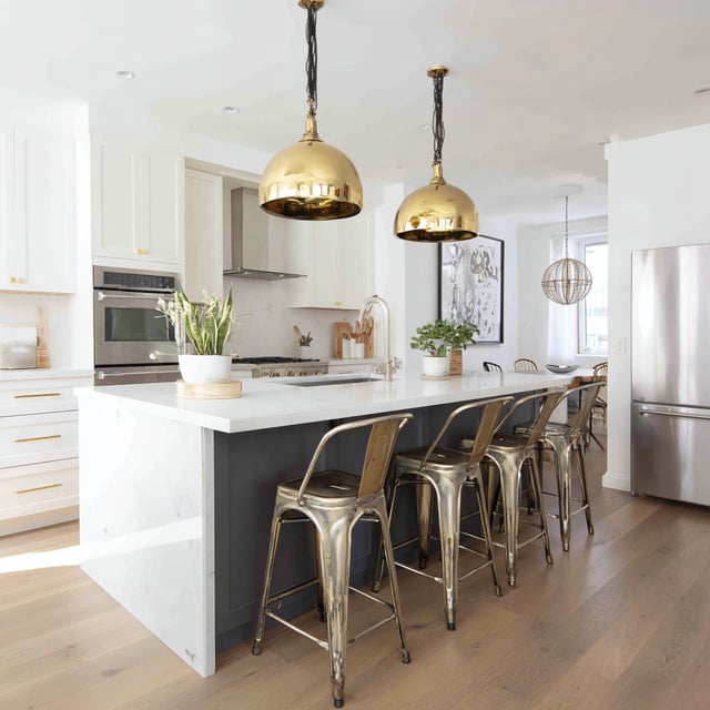 Modern kitchen with gold pendants, marble island, and stools.