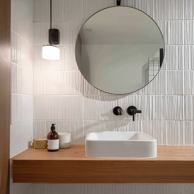 Modern white bathroom with wood vanity and round mirror.