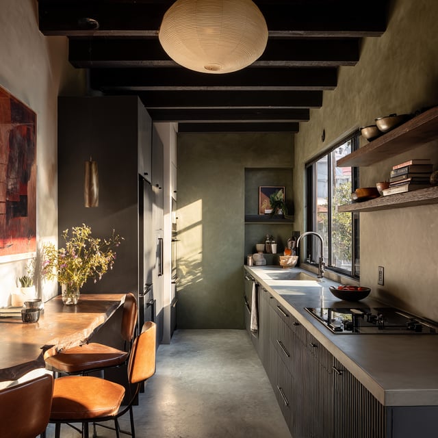 Moody narrow kitchen with green walls and wood beam ceiling.